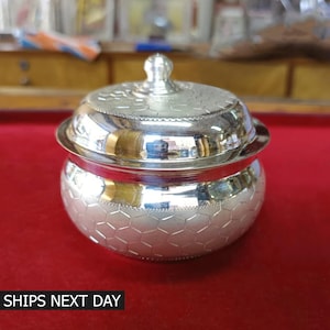 May include: A silver container with a lid, featuring a hexagonal pattern. The container is round and has a smooth, polished finish.