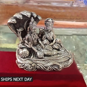 May include: A silver statue of a Hindu deity couple, sitting on a serpent throne. The statue is intricately detailed and has a traditional design.