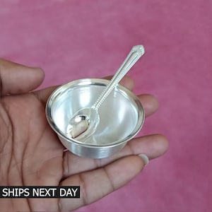 May include: A small, shiny silver bowl with a matching spoon inside. The spoon has a decorative handle. The bowl and spoon are held in a hand against a pink background. The text "SHIPS NEXT DAY" is at the bottom.