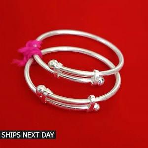 May include: Two silver baby bangles with a double band design and small round accents. The bangles are stacked on top of each other.