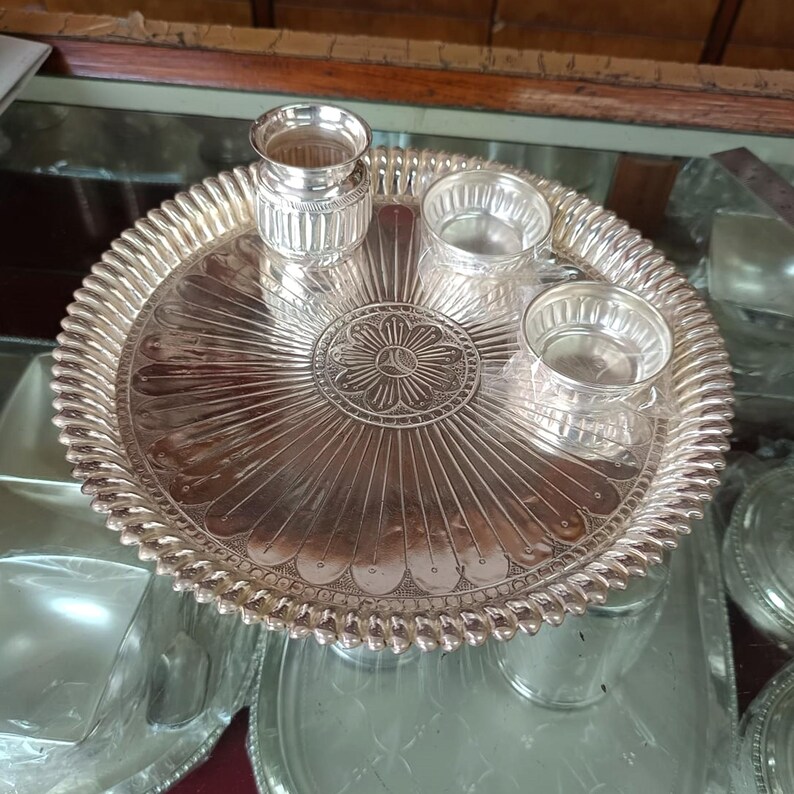 May include: A silver serving tray with a decorative design and three small silver bowls. The tray has a raised edge and a scalloped design.