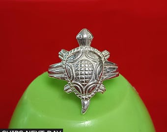 May include: A silver-colored ring with a turtle design. The turtle has a detailed shell and head, with a textured pattern. The ring is set against a green background with a red backdrop. The text "SHIPS NEXT DAY" is visible.