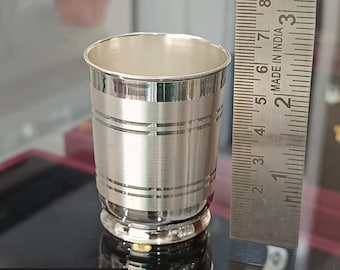 May include: A small, shiny silver cup with horizontal etched lines. The cup has a rounded base and a smooth, polished rim. A ruler is placed next to the cup, showing measurements in inches. The text "SHIPS NEXT DAY" is at the bottom.