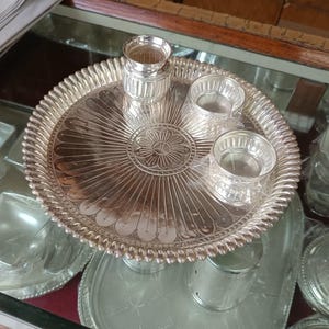May include: A silver serving tray with a decorative design and three small silver bowls. The tray has a raised edge and a scalloped design.