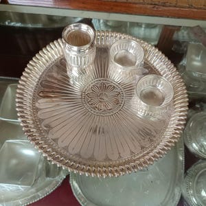 May include: A silver serving tray with a decorative floral design in the center. The tray has three smaller silver bowls, perfect for serving small snacks or condiments.