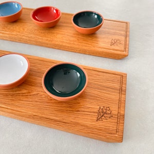Könnte beinhalten: Zwei Holz-Serviertabletts mit einem eingravierten Blattdesign auf jedem. Die Tabletts sind mit fünf kleinen Keramikschalen gefüllt, jede mit einer anderen Farbe: blau, rot, weiß, grün und grün.