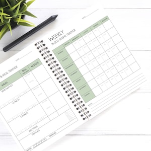 May include: A white spiral bound notebook with a green and black cover. The cover has the text "Daily Blood Sugar & Meal Tracker" and "Weekly Blood Sugar Tracker". The notebook has a section for daily meal tracking and a section for weekly blood sugar tracking.