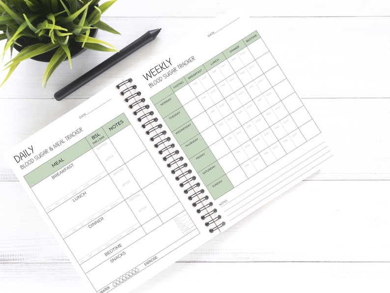 May include: A white spiral bound notebook with a green and black cover. The cover has the text "Daily Blood Sugar & Meal Tracker" and "Weekly Blood Sugar Tracker". The notebook has a section for daily meal tracking and a section for weekly blood sugar tracking.