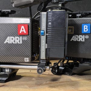 Peut inclure: Deux boîtiers de caméra ARRI en fibre de carbone noire avec une étiquette carrée rouge portant la lettre A et une étiquette carrée bleue portant la lettre B. Une monture de batterie Bebob Cine VMM-ALM est fixée entre les deux unités.