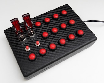 May include: A black gaming controller with a carbon fiber pattern. It has 18 red buttons and two red toggle switches.