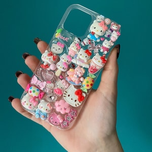Può includere: Custodia trasparente per telefono decorata con numerose figure 3D di Hello Kitty in varie pose e abiti. La custodia presenta dettagli rosa, rossi, blu e bianchi, tra cui fiocchi, stelle e coni gelato. La parola "sweet" è visibile.