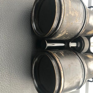 K&ouml;nnte beinhalten: Ein Paar vintage schwarze Ferngl&auml;ser mit Messingakzenten. Die Ferngl&auml;ser haben einen abgenutzten, gealterten Look und sind scharf.
