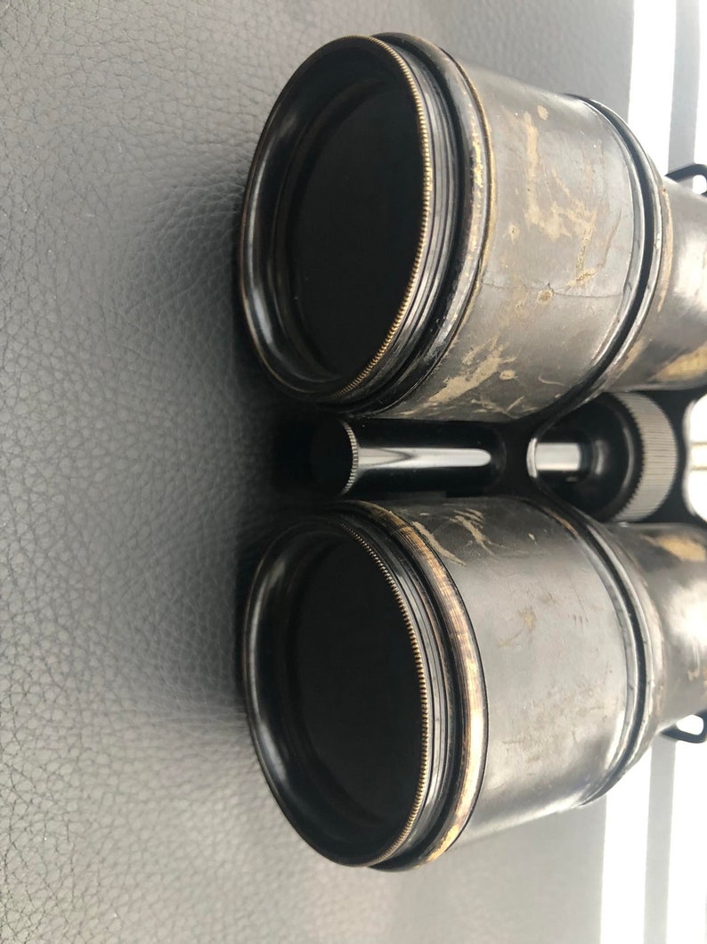 K&ouml;nnte beinhalten: Ein Paar vintage schwarze Ferngl&auml;ser mit Messingakzenten. Die Ferngl&auml;ser haben einen abgenutzten, gealterten Look und sind scharf.