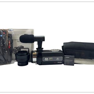 Pode incluir: Um kit de câmera de vídeo digital 4K preto com acessórios, incluindo um microfone, uma lente, uma bateria e uma bolsa de transporte. A câmera tem um detalhe prateado e o texto "4K" na frente. O kit também inclui um controle remoto e um manual.