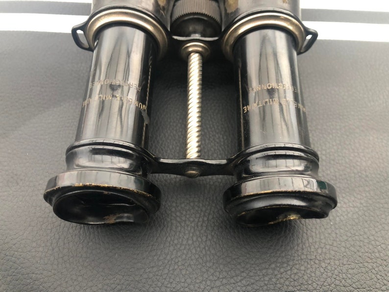 K&ouml;nnte beinhalten: Vintage-Fernglas in Schwarz mit einem silberfarbenen Mittelgelenk und graviertem Text auf den Rohren, der "REG. NO. 151974" und "REG. NO. 151974" lautet.