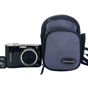 May include: A black Samsung digital camera with a 5x zoom lens, a gray Samsonite camera bag, and an 8GB SD card.