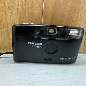 Könnte beinhalten: Eine schwarze Traveler AF mini Kamera mit einem silbernen Objektiv und einer Funktion zur Reduzierung von Rote-Augen-Effekten. Die Kamera hat einen schwarzen Gurt.