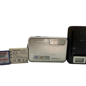 Cámara digital compacta Samsung Digimax i5 de 5 MP con zoom óptico de 3X, pantalla de 2,5 pulgadas, flash de seguridad, tarjeta de memoria de 2 GB, batería, cargador y correa de mano.