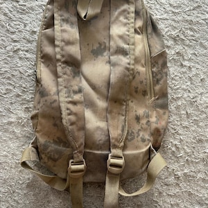 May include: A camouflage-patterned backpack with adjustable straps and a zipped pocket on the side.