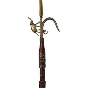 May include: A polearm featuring a central brass spearhead, a curved hook, and a stylized brass elephant figure attached to the side. The shaft is constructed from dark reddish-brown wood with horizontal brass bands and decorative yellow line accents.