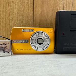 May include: A yellow Olympus digital camera with a 7.1 megapixel lens and a black Olympus battery charger.