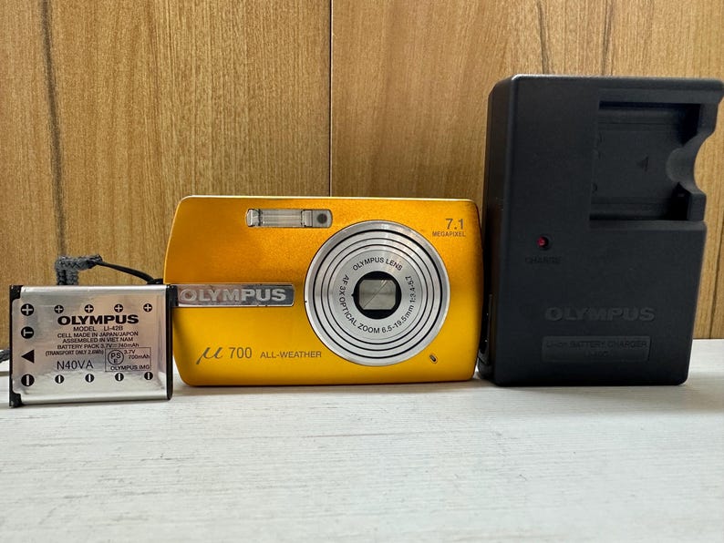 May include: A yellow Olympus digital camera with a 7.1 megapixel lens and a black Olympus battery charger.