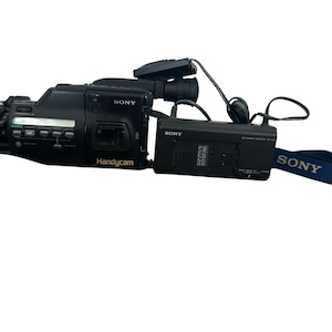 May include: Black Sony Handycam with a lens, buttons, and a blue strap. The camera has the word "SONY" printed on the side and on the strap. The word "Handycam" is printed on the side of the camera.
