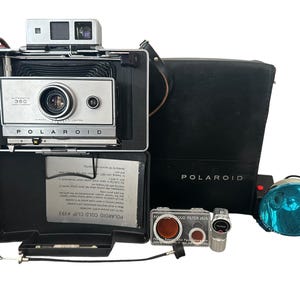 Puede incluir: Una cámara vintage Polaroid Automatic 360 Land Camera con fuelle negro, placa frontal plateada y visor superior. Incluye un estuche de transporte negro, un reflector de flash azul, un kit de filtros, un disparador de cable y un accesorio cold clip.