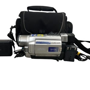 May include: Silver JVC digital video camera with a black carrying bag and a black battery charger. The camera has a 300x zoom lens and a digital night scope feature. The bag has a shoulder strap.