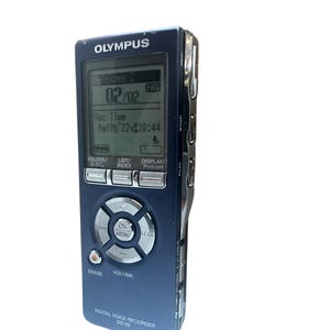 Può includere: Un registratore vocale digitale Olympus DS-50 blu con uno schermo di visualizzazione nero e argento. Lo schermo mostra la data, l'ora e il tempo di registrazione. Il registratore ha pulsanti per cartella, elenco, indice, visualizzazione, riproduzione, arresto, cancellazione, volume e OK/menu.