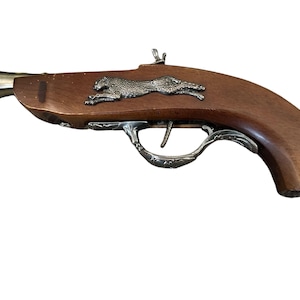 Könnte beinhalten: Eine Spielzeugpistole aus Holz mit einem silbernen Geparden-Design auf der Oberseite. Die Pistole hat einen silbernen Abzug und einen braunen Holzgriff.