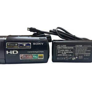 May include: Black Sony Handycam with a wide-angle lens and a compact power adapter. The camera has "HD AVCHD" and "1080" labels. The power adapter has the text "AC-L200 COMPACT POWER ADAPTER".