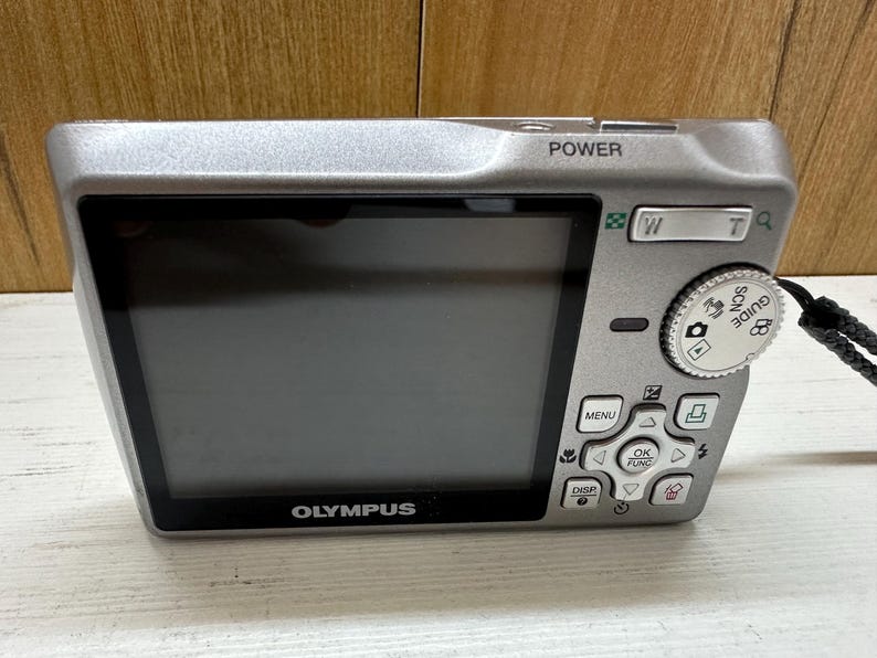 May include: A silver Olympus digital camera with a black screen and buttons. The camera has a zoom lens and a built-in flash. The camera is in good condition and appears to be used.