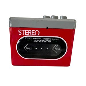 May include: A red and gray vintage stereo personal cassette player. The player has the word "STEREO" in white text, along with "STEREO PERSONAL CASSETTE PLAYER HIGH RESOLUTION". It features play and fast forward buttons.