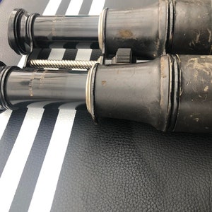 K&ouml;nnte beinhalten: Ein Paar vintage schwarze Ferngl&auml;ser mit einem silbernen Einstellknopf. Die Ferngl&auml;ser haben eine abgenutzte Lederoptik und sind in gutem Zustand.