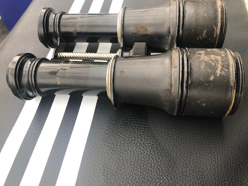 K&ouml;nnte beinhalten: Ein Paar vintage schwarze Ferngl&auml;ser mit einem silbernen Einstellknopf. Die Ferngl&auml;ser haben eine abgenutzte Lederoptik und sind in gutem Zustand.