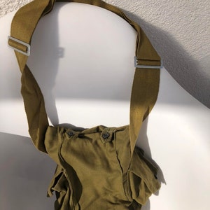 Puede incluir: Un bolso de hombro de lona verde con dos bolsillos y una correa larga. El bolso tiene dos botones en la parte delantera.