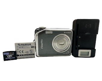 May include: A silver Fujifilm FinePix digital camera with a lens, flash, and buttons, accompanied by a battery, charger, and an Olympus XD Picture Card. The battery pack reads "NP-40".