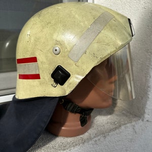 Op de afbeelding: Een gele brandweerhelm met een rode en witte streep, een zilveren reflecterende streep en een helder vizier.