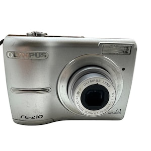 May include: A silver Olympus FE-210 digital camera with a 7.1 megapixel resolution and a 3x optical zoom lens.
