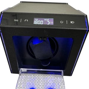 Puede incluir: Un enrollador de relojes negro con una tapa de acrílico transparente. El enrollador tiene una pantalla digital que muestra "TPD 1800" y un ajuste de modo. El enrollador tiene luces LED azules alrededor de los bordes y en el interior.