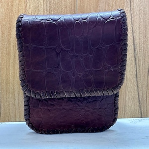 Puede incluir: Una cartera de cuero marrón oscuro con un borde cosido y un patrón de piel de cocodrilo.