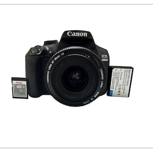 May include: Black Canon EOS 1300D DSLR camera with a YONGNUO lens, a 32GB Hama SD card, and a battery pack. The camera lens is marked EF 35mm 1:2. The camera and accessories are on a white background.