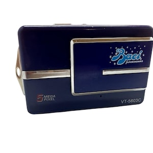 May include: A navy blue digital camera with a silver trim. The camera has the text "Baci PERUGINA®" in a light blue script and the words "5 MEGA PIXEL". The model number "VT-5603C" is also visible.