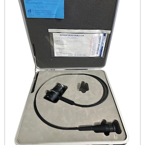 May include: An open silver medical equipment case with a black endoscope inside. The case has a blue paper with the word "OLYMPUS" and "ENDOSCOPE" printed on it. The case also contains a repair information sheet.