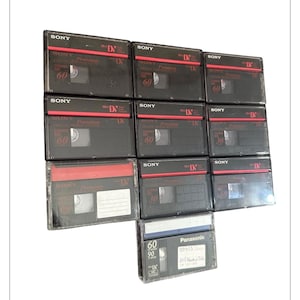 Könnte beinhalten: Eine Ansammlung schwarzer Sony MiniDV-Videokassetten, einige mit roten Akzenten, angeordnet auf weißem Hintergrund. Die Kassetten sind mit "60" und "30" beschriftet, was die Aufnahmezeit in Minuten angibt. Eine Panasonic MiniDV-Kassette ist ebenfalls zu sehen.