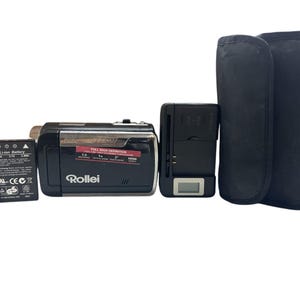 May include: A black Rollei digital video camera with a battery, SD card, charger, and a black carrying case. The camera has a silver accent and a red sticker that says "FULL HIGH DEFINITION". The SD card is a Lexar 1GB.