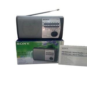 May include: A Sony ICF-403S portable radio with a silver speaker grille, black casing, and an extendable antenna. The radio is displayed with its original green and white product box and a white instruction manual labelled FM/MW/SW 3 Band Radio.