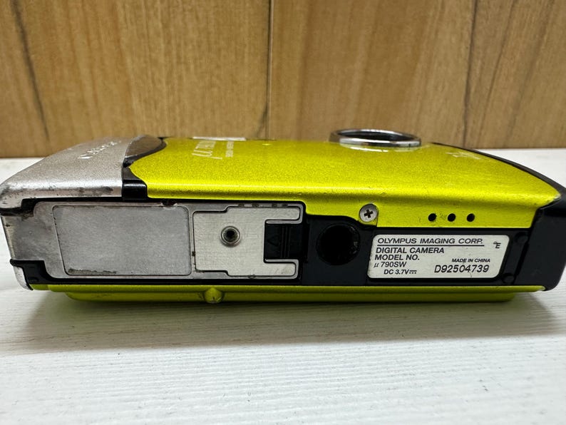 May include: A yellow Olympus digital camera with a silver top and black lens. The camera has a model number of 790SW and a serial number of D92504739.