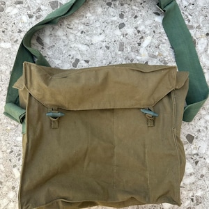 May include: An olive green canvas messenger bag with a matching adjustable shoulder strap. The bag has a flap closure secured by two plastic toggles. The rectangular bag appears to be made of durable material.